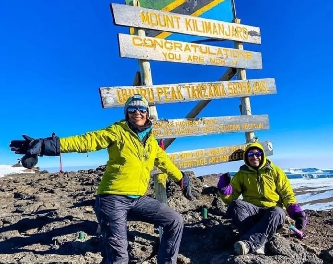 Couple reaching the summit of Mount Kilimanjaro, celebrating at Uhuru Peak in Tanzania after completing their climbing adventure together.