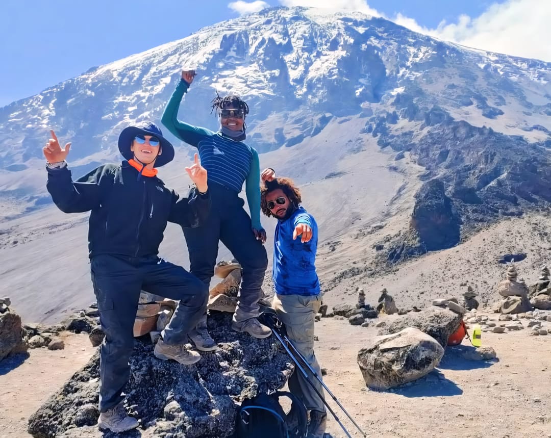 Climbers taking a group photo at a scenic point on Mount Kilimanjaro during the Umbwe Route trek in Tanzania, surrounded by mountain landscape.