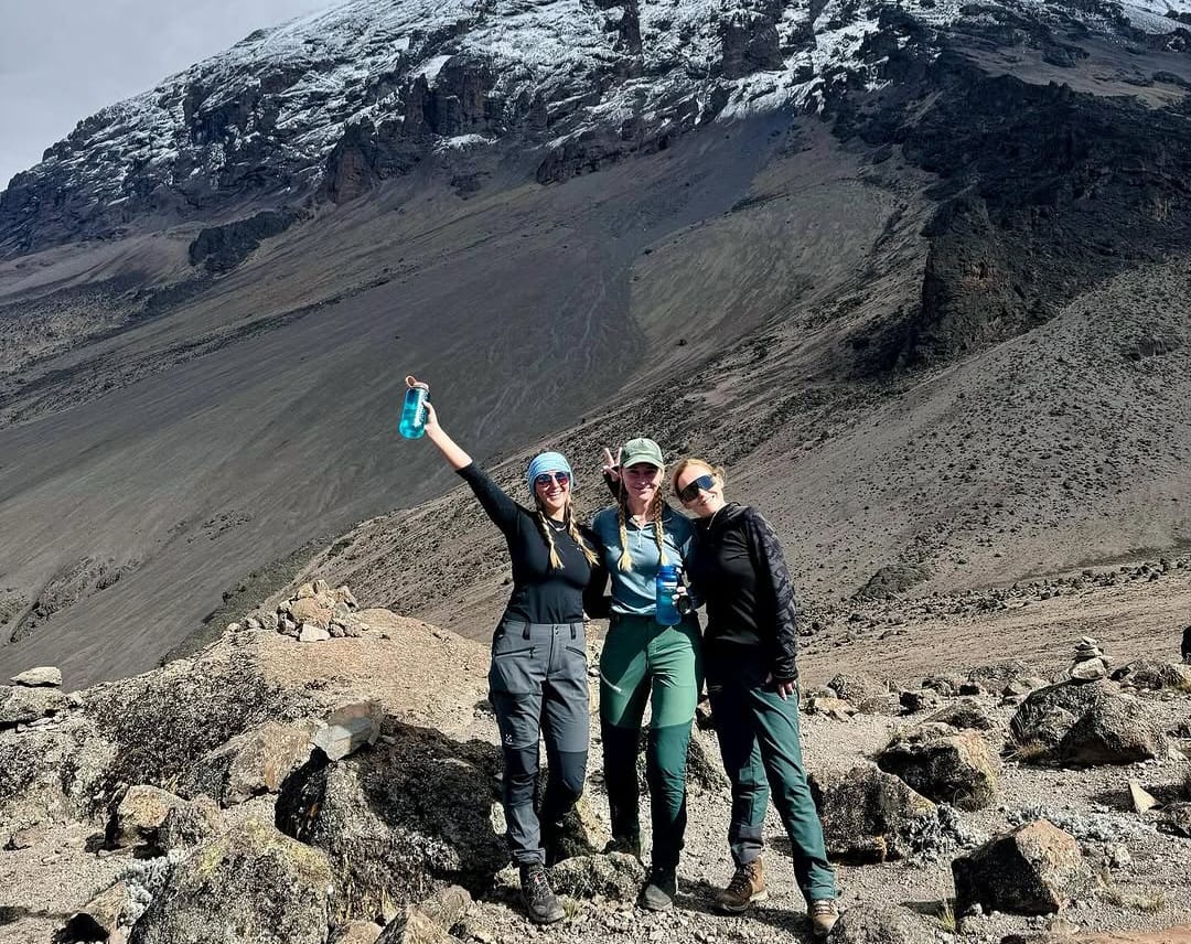 Three friends taking a photo while climbing Mount Kilimanjaro via the Lemosho Route, enjoying scenic mountain views in Tanzania.