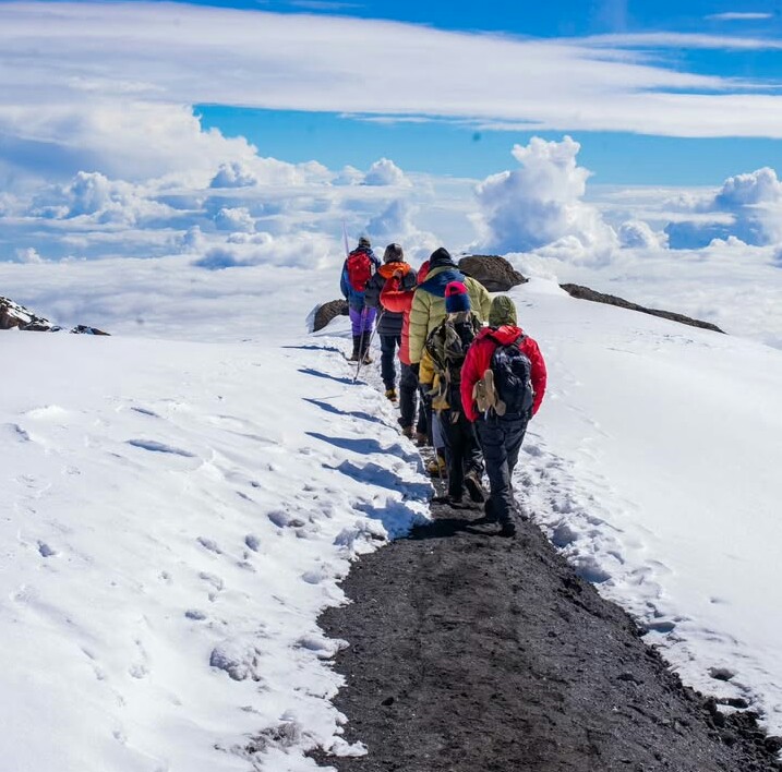 Beginner climber ascending Mount Kilimanjaro with guide and trekking poles against scenic Tanzanian landscape.