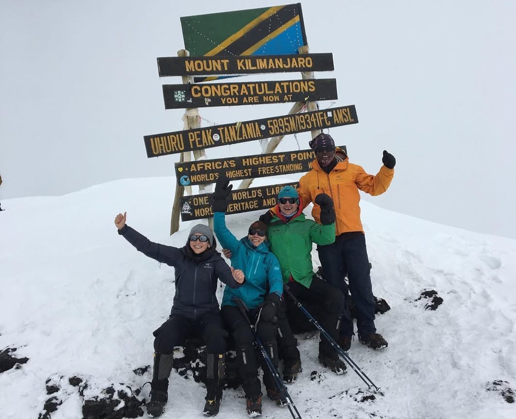 Climbers standing at the summit of Mount Kilimanjaro at Uhuru Peak, celebrating success above the clouds in Tanzania after a challenging ascent.