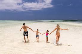 Couple walking hand-in-hand on Zanzibar’s white sandy beach with turquoise waters and a sunset in the background.